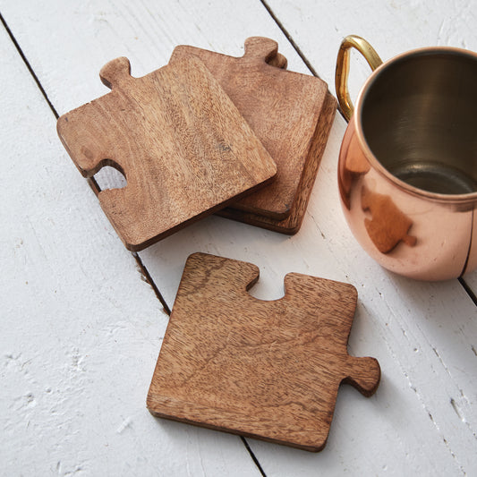 Four wooden puzzle coasters assembled into a square mat on a coffee table, showcasing their unique and whimsical design.