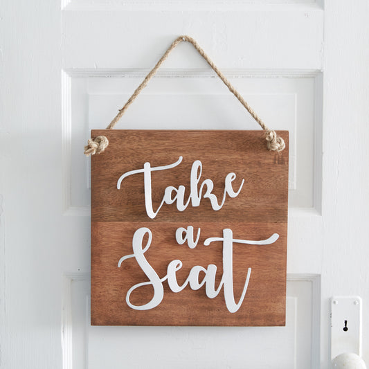 Wooden wall sign with metal lettering reading "Take A Seat," featuring a jute rope for hanging, adding humor to bathroom decor.