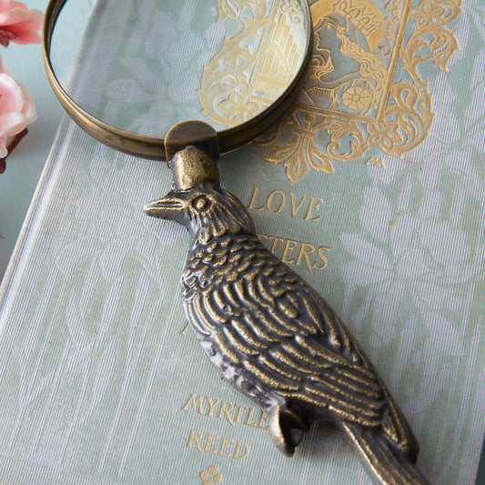 Raven Magnifying Glass with antique brass finish on a desk, showcasing its elegant design and sophisticated aesthetic.