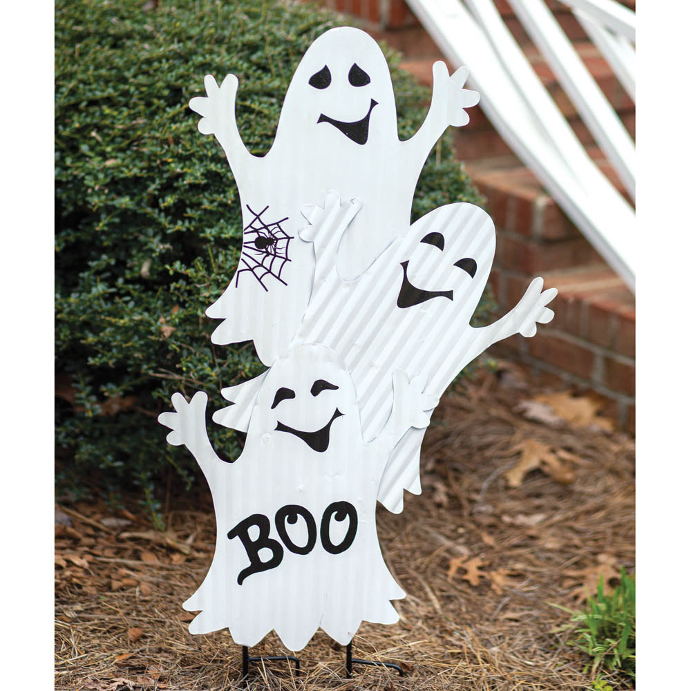 Three ghost figures crafted from corrugated metal, each with a playful expression, stand on dual stakes in a garden setting.