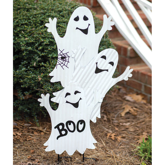 Three ghost figures crafted from corrugated metal, each with a playful expression, stand on dual stakes in a garden setting.