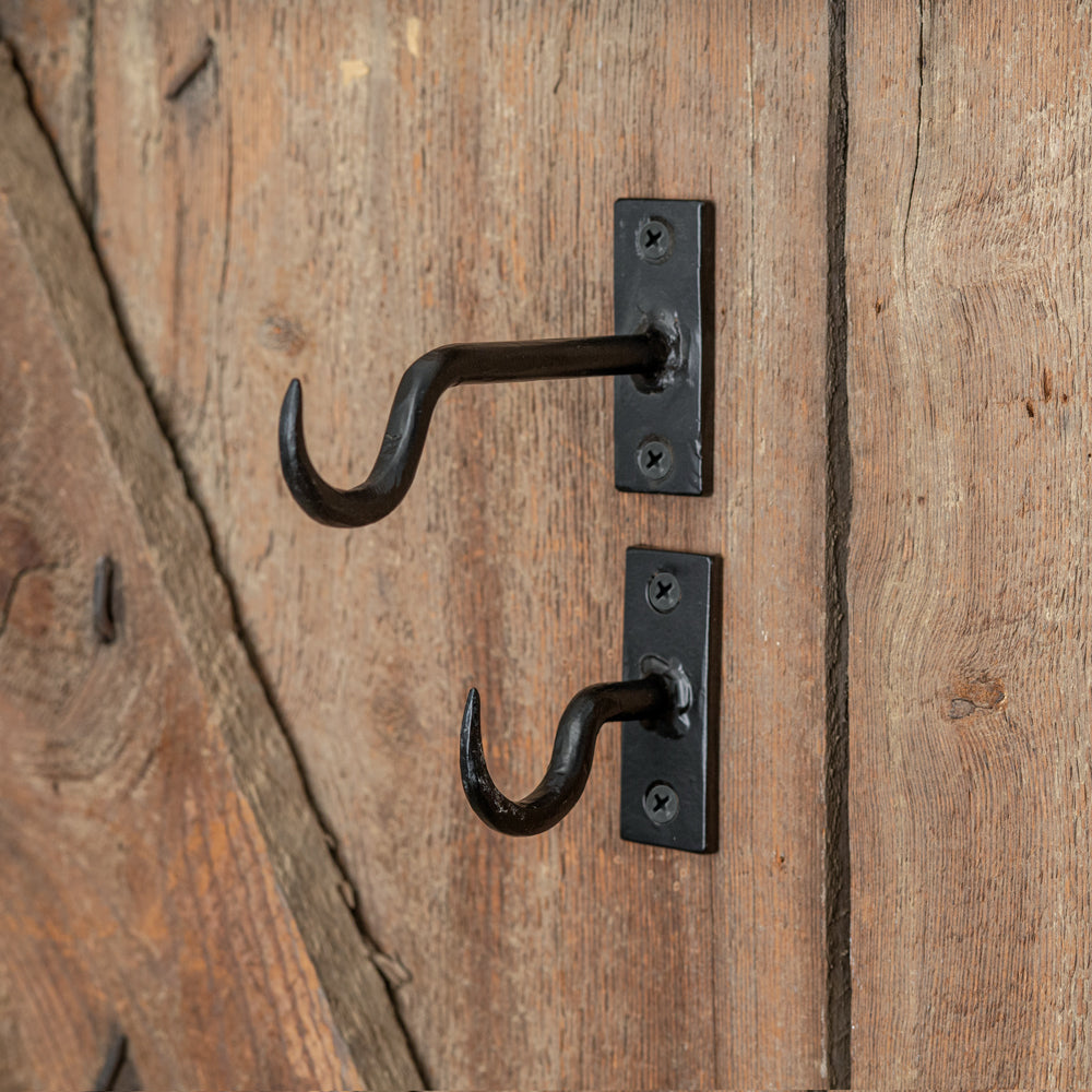 Two sleek black cast iron hooks with screw holes, perfect for hanging coats or plants, adding style to any space.