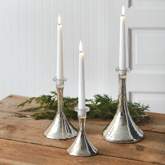 Three silver mercury glass taper candle holders with a shimmering finish, varying in height, creating an elegant table setting.