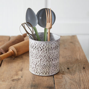 A metal utensil holder with stamped wildflower designs, holding various kitchen utensils, adding elegance and organization.