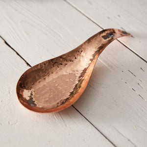 Hand-hammered copper spoon rest on a kitchen counter, showcasing its elegant design and artisanal craftsmanship.