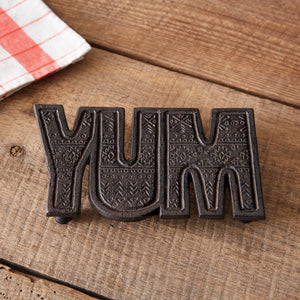 Rustic cast iron trivet with "Yum" text, showcasing farmhouse charm; perfect for protecting countertops and enhancing decor.