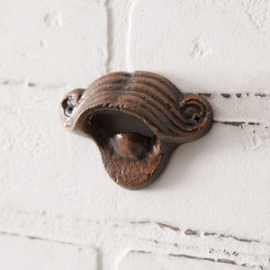 Mustache-shaped cast iron bottle opener mounted on a wall, showcasing its quirky design and sturdy build for easy bottle opening.