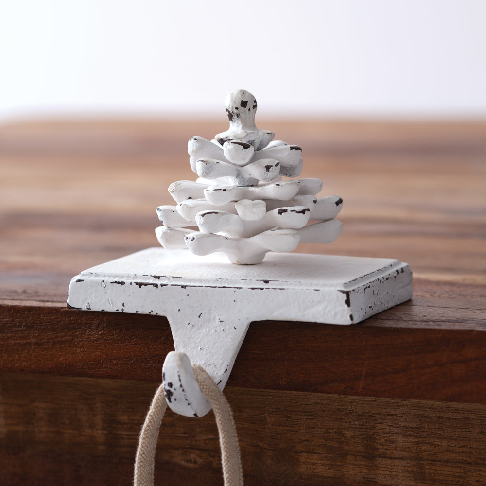 Cast iron pinecone stocking holder with a whitewashed finish, adding rustic charm and elegance to holiday mantel decor.